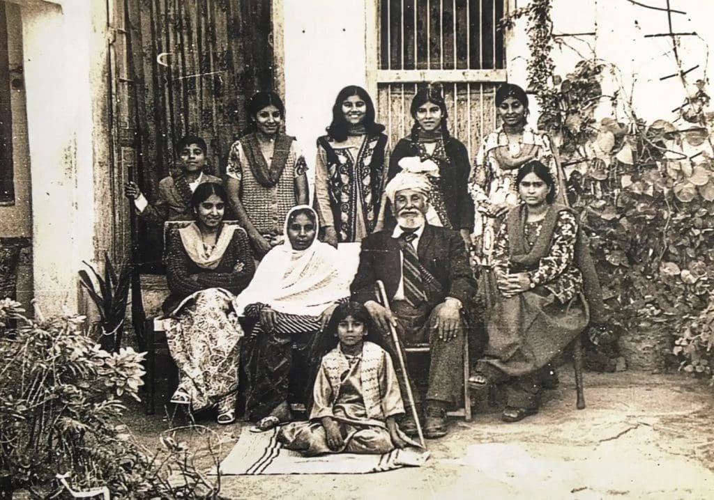 Black and white photo of an elder gentleman with a turban sitting with his family.