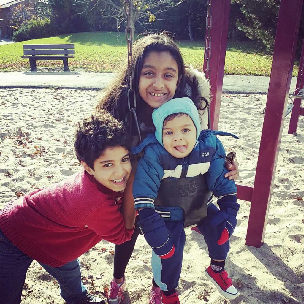 Three young kids at the park enjoying the swing.