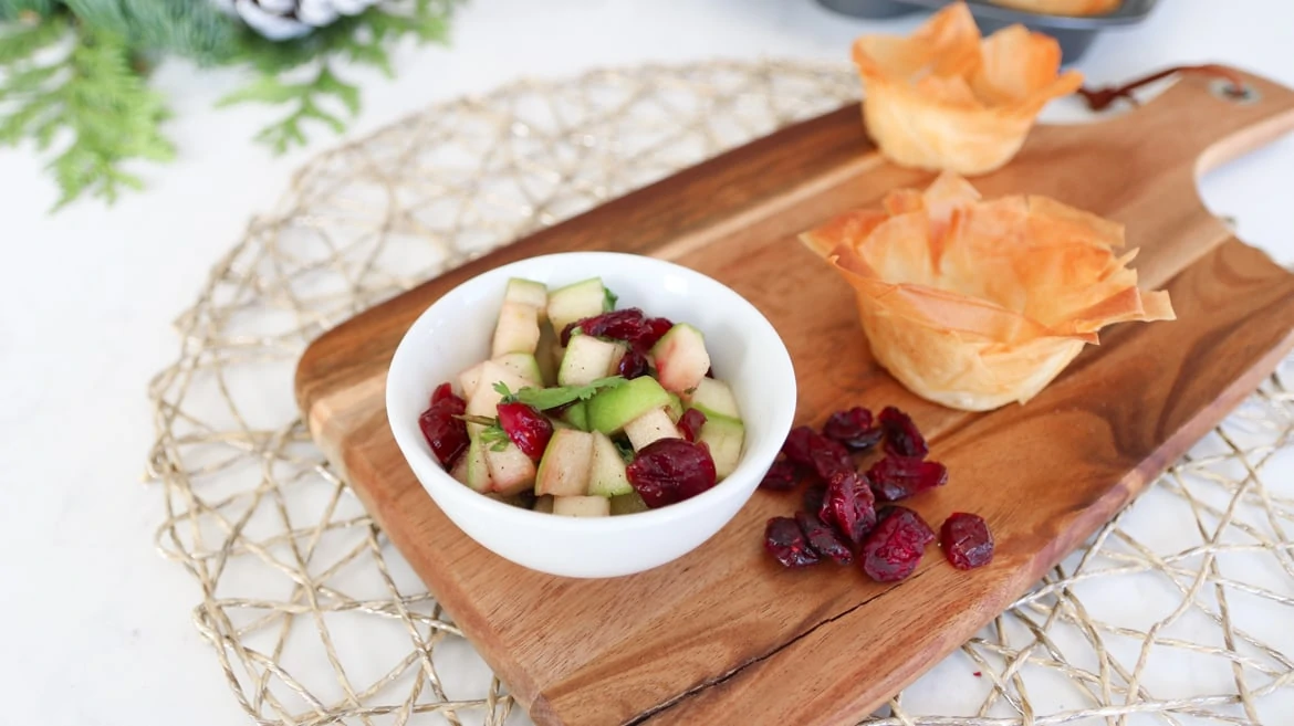 bowl of cranberry and apple salsa with filo cups on a wooden board with dried cranberries