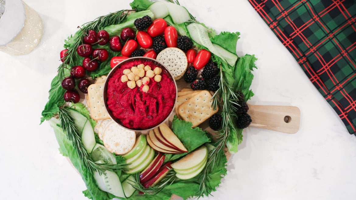 colourful platter of fruits and vegetables with crackers around a bowl of beet hummus