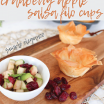 bowl of cranberry and apple salsa with filo cups on a wooden board with dried cranberries