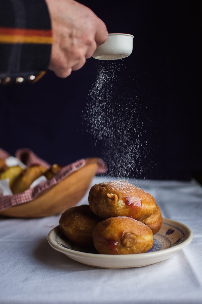 icing sugar being dusted on donuts on a plate
