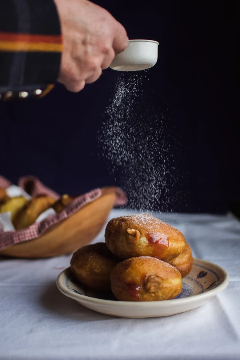 icing sugar being dusted on donuts on a plate