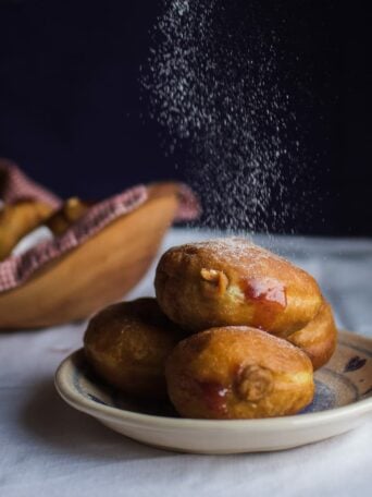 icing sugar being dusted on donuts on a plate