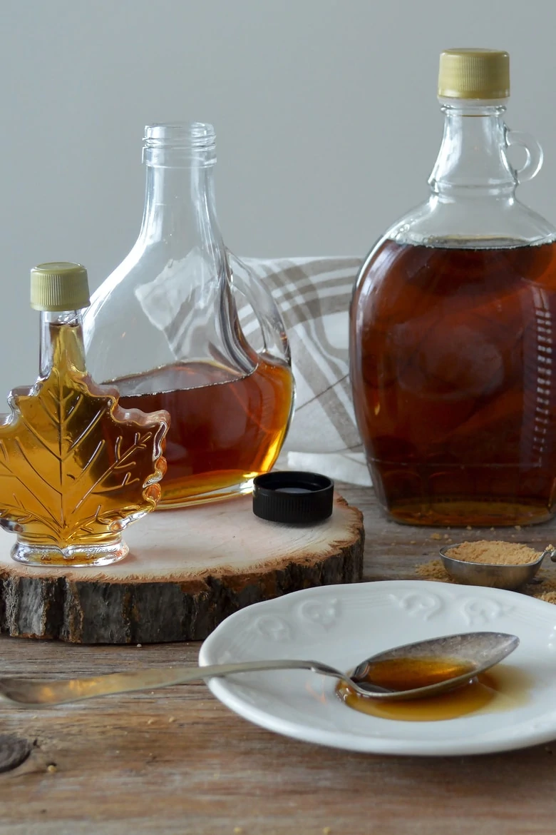 three bottles of maple syrup with a spoon of maple syrup