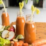 bottles of homemade carrot juice with raw ingredients around the three bottles