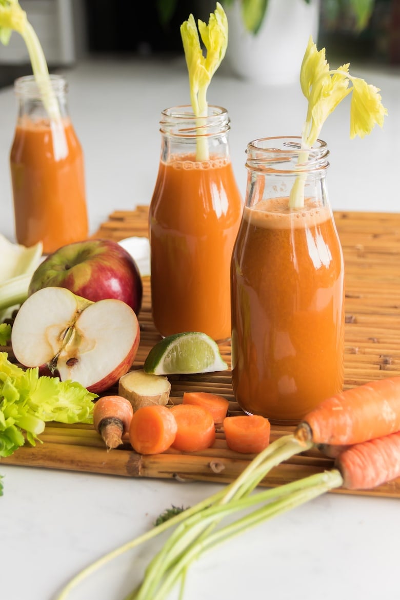 bottles of homemade carrot juice with raw ingredients around the three bottles