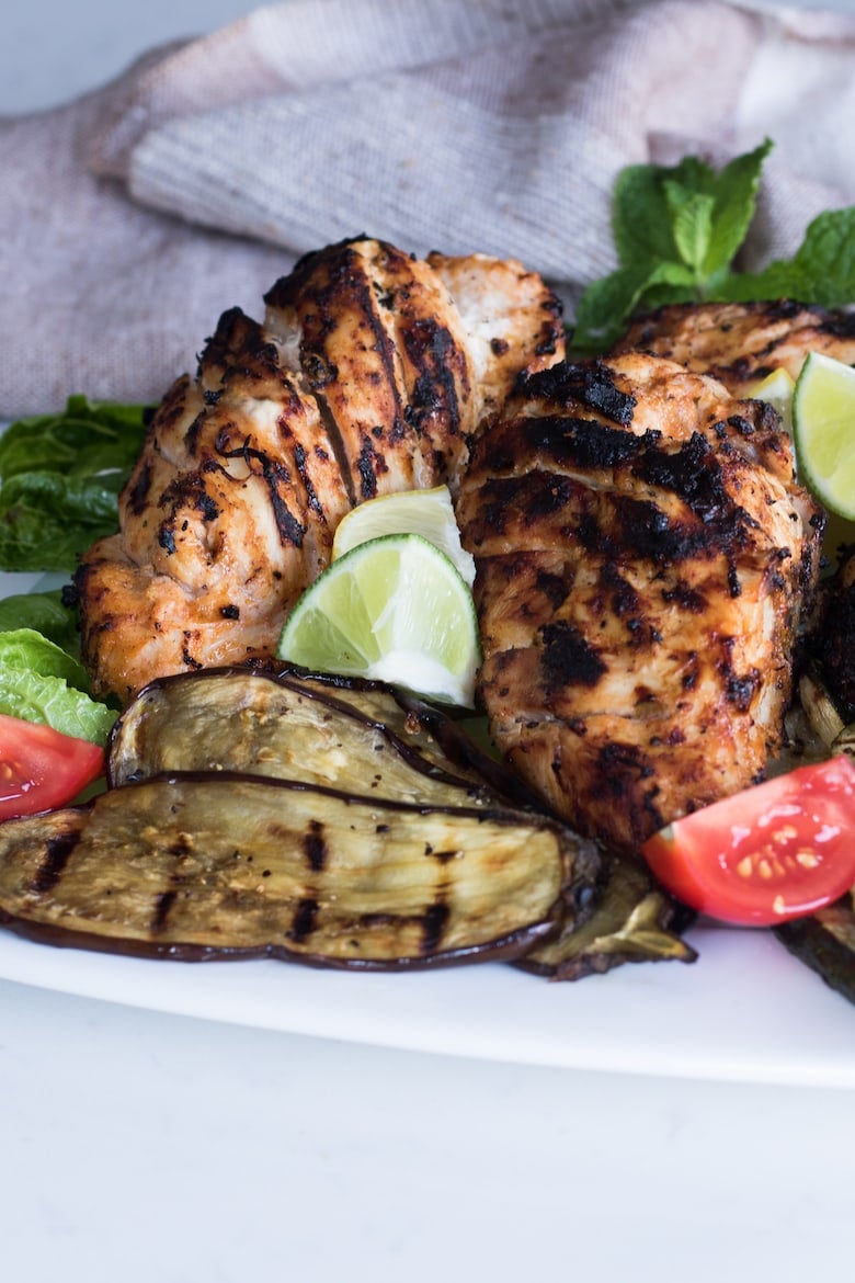 grilled tandoori chicken served with grilled vegetables and lime slices.