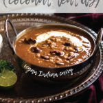daal makhani in a silver bowl on a round tray on top of a maroon velvet cloth with maroon flowers and roti in the background