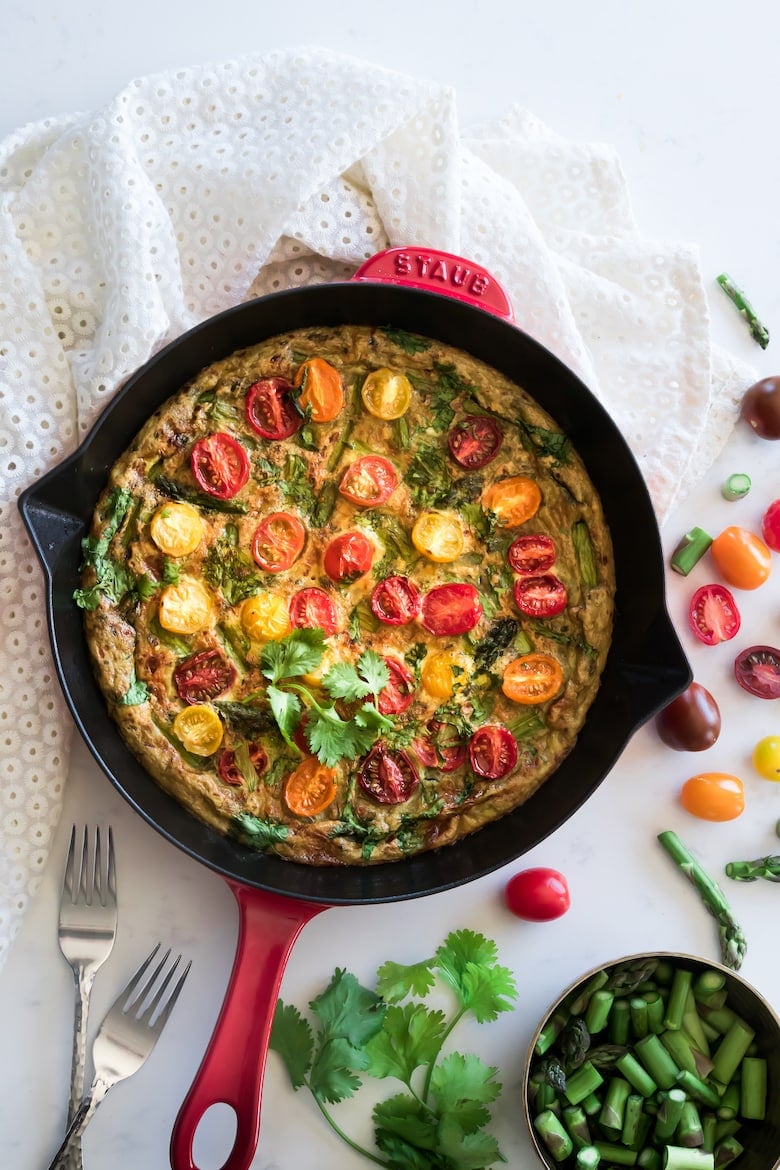 Asparagus Frittata topped with colorful tomatoes in a red pan on a table cloth