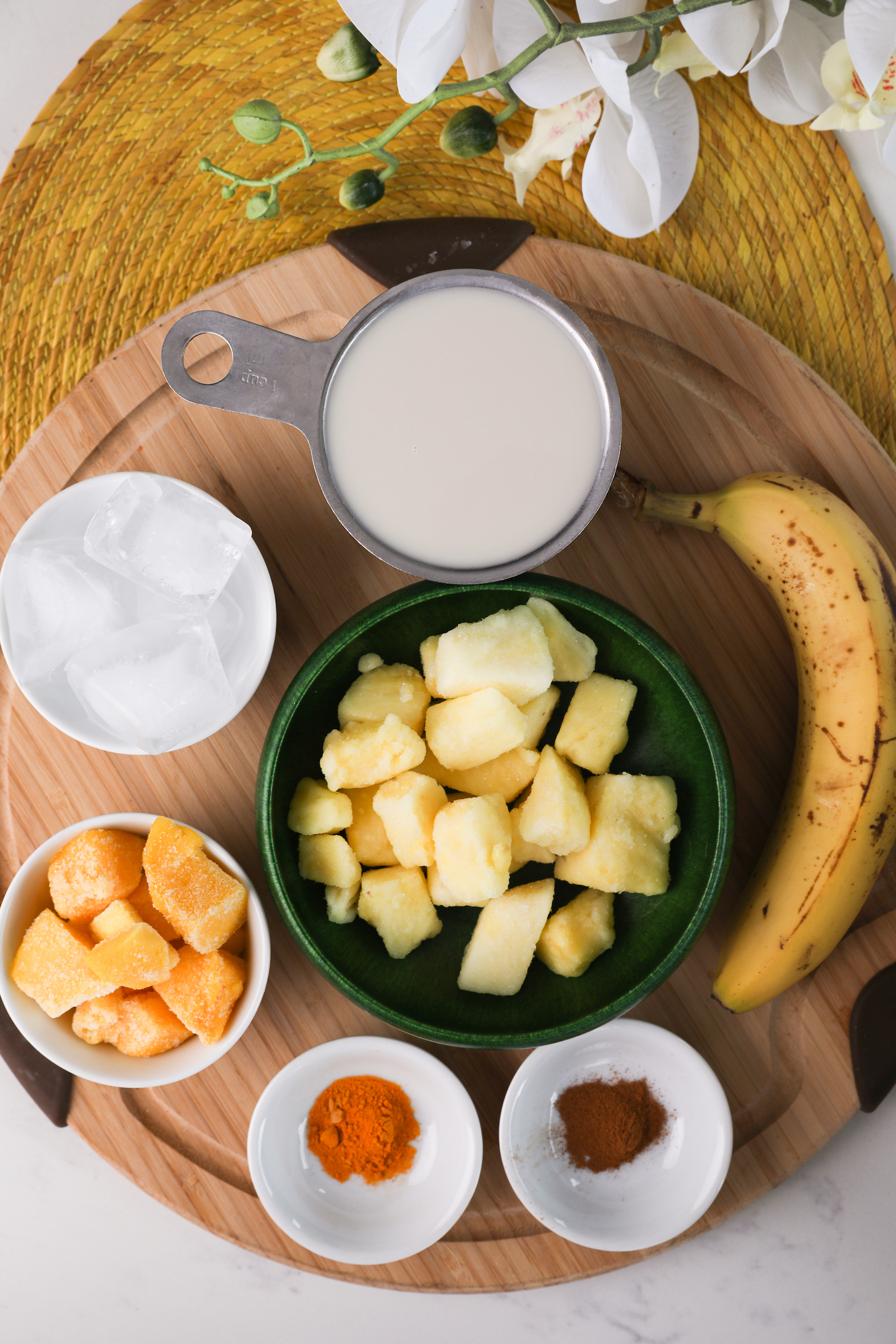 Food ingredients like pineapple and mango chunks, banana and milk arranged on a wooden board.