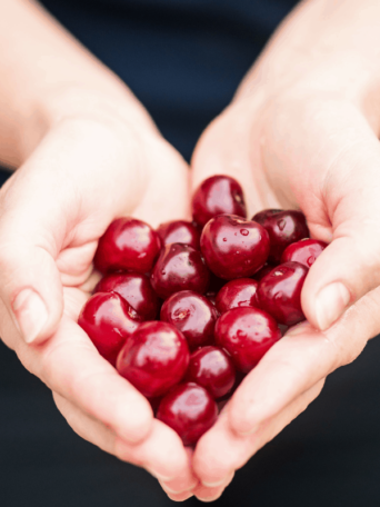a person holding a handful of cherries in the shape of a heart