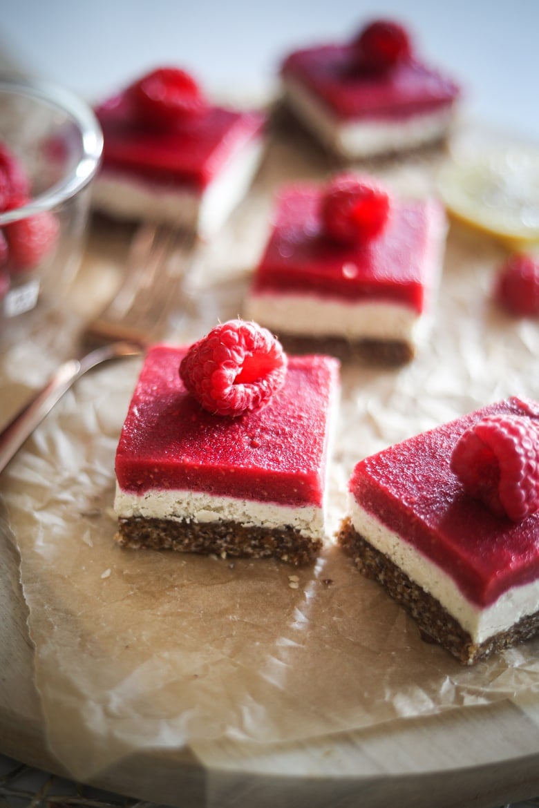 five raspberry vegan bars with a raspberry on each slice, placed on a wooden board
