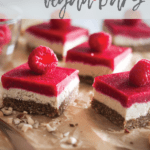 five raspberry vegan bars with a raspberry on each slice, placed on a wooden board with sprinkle of chopped nuts.