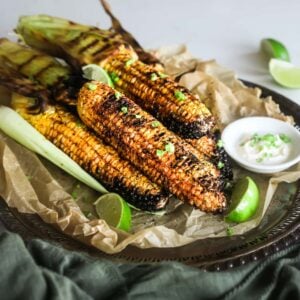 pile of bbq corn coated in spices on a tray with lime segments and dipping sauce