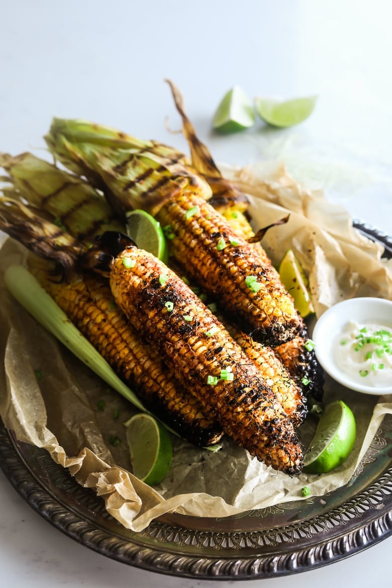 pile of bbq corn coated in spices on a tray with lime segments and dipping sauce