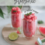 two glasses of watermelon slushie surrounded by pieces of lime and watermelon