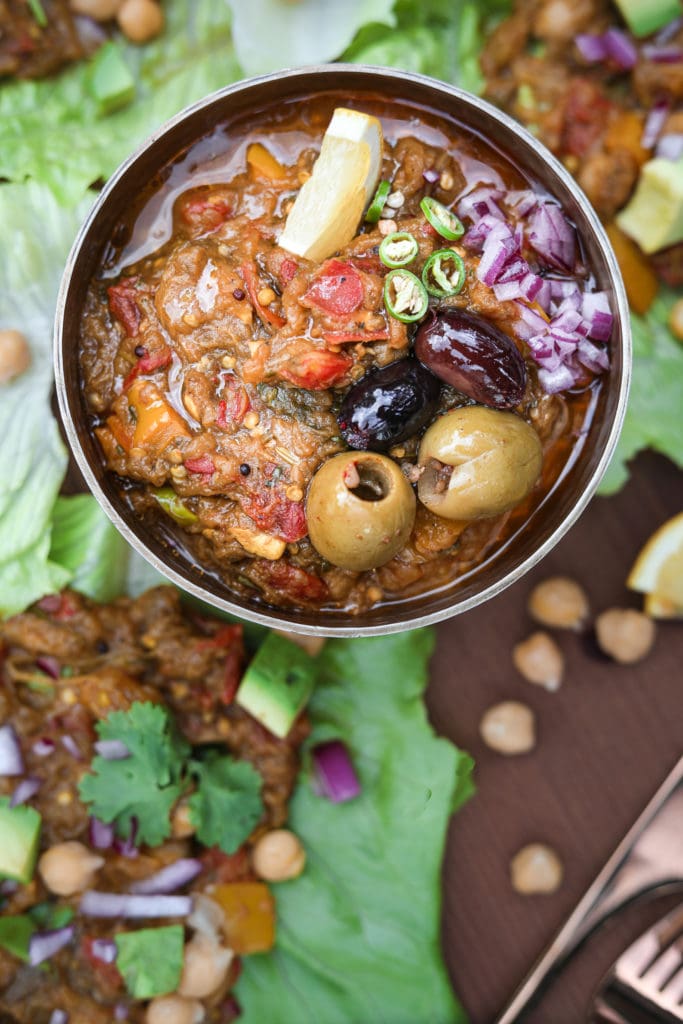 a bowl of baingan bharta topped with olives and chilli with lettuce leaves filled with baingan bharta (Indian eggplant recipe) withlettuce leaves filled with baingan bharta (Indian eggplant recipe) with lettuce leaves filled with bharta in the background