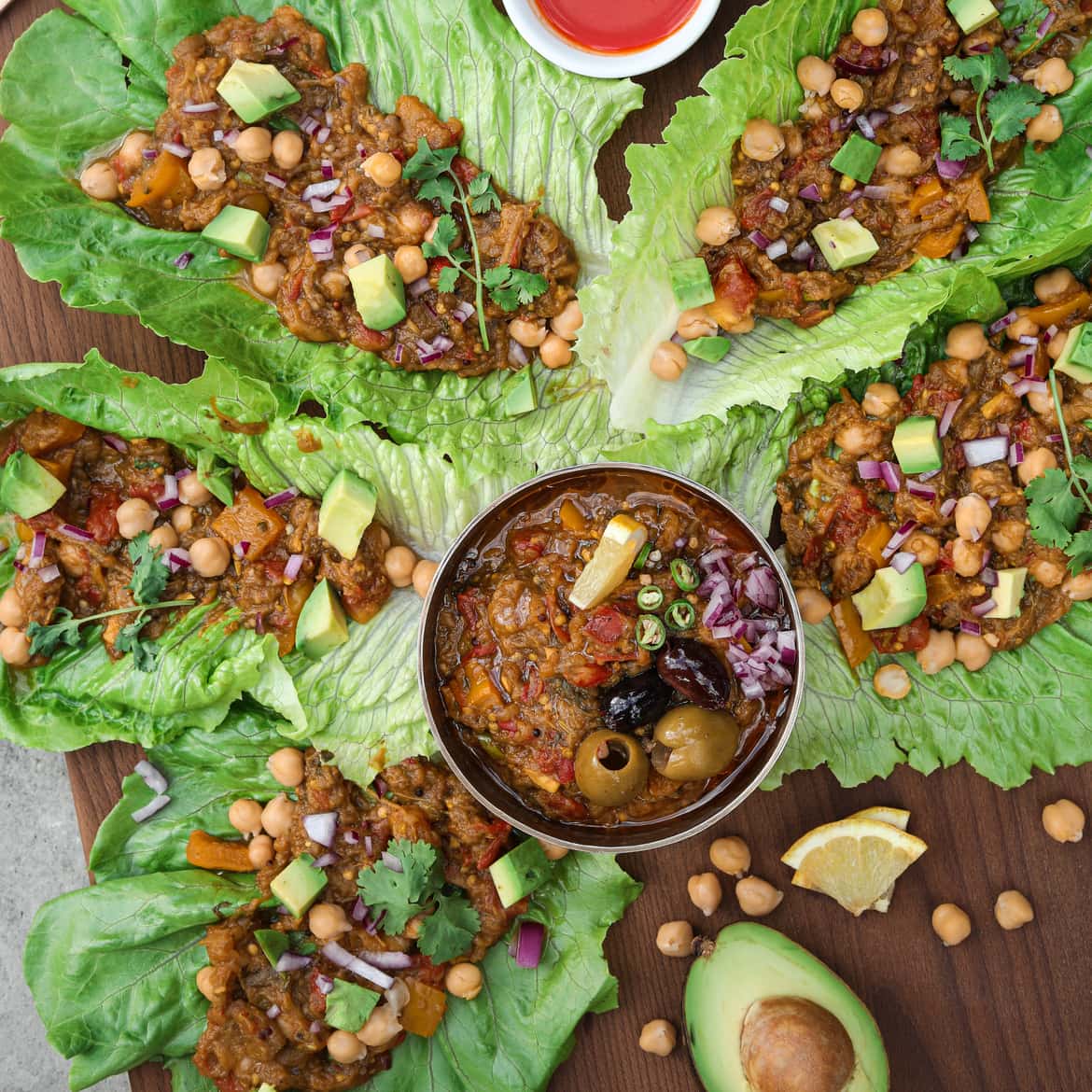 lettuce leaves filled with baingan bharta (Indian eggplant recipe) with a bowl of baingan bharta in the center.