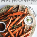 pile of baked sweet potato wedges on a wooden round board with two bowls of dipping sauces