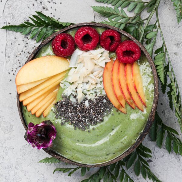healthy green smoothie bowl topped with sliced peaches, raspberries, coconut and chia seeds