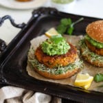 Two Desi Pumpkin Bean Burgers on a bed of alfalfa microgreens topped with guacamole in burger buns on a black tray