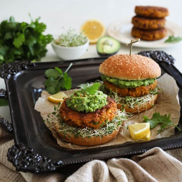 Two Desi Pumpkin Bean Burgers on a bed of alfalfa microgreens topped with guacamole in burger buns on a black tray