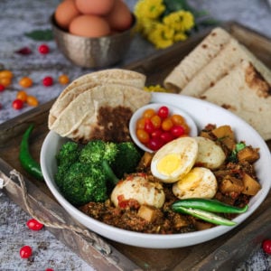 Egg curry recipe with turnips in a bowl with roti, broccoli, and tomatoes in a gold tray