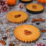 a row of homemade pumpkin pies topped with pecans with pumpkins in the background