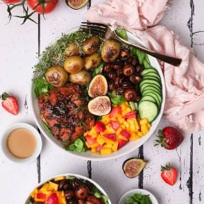 Easy and healthy recipe of colorful bowl of soy maple glazed salmon fillet served with potatoes, mushrooms, mango and strawberry salad on a bed of lettuce