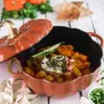 Afghan pumpkin curry in a pumpkin cocotte surrounded by fresh pumpkins, herbs and naan bread