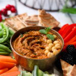 Holiday veggie dip with chcikpeas on top surrounded by fruits and vegetables