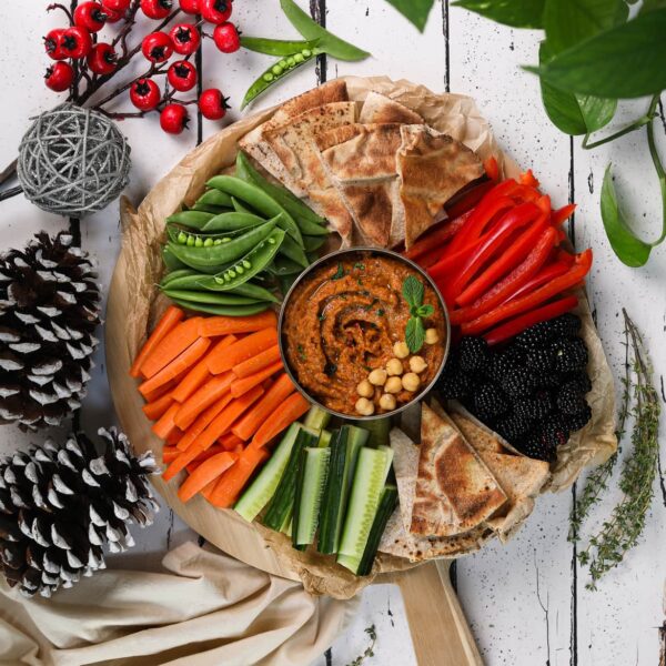 A colourful holiday veggie dip surrounded by carrots, cucumbers, peppers, snap peas, naan bread and blackberries