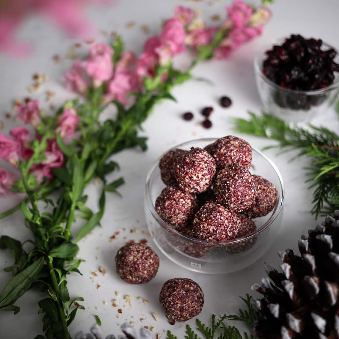 bowl filled with cranberry energy bites with pink flowers and dried cranberries in the background