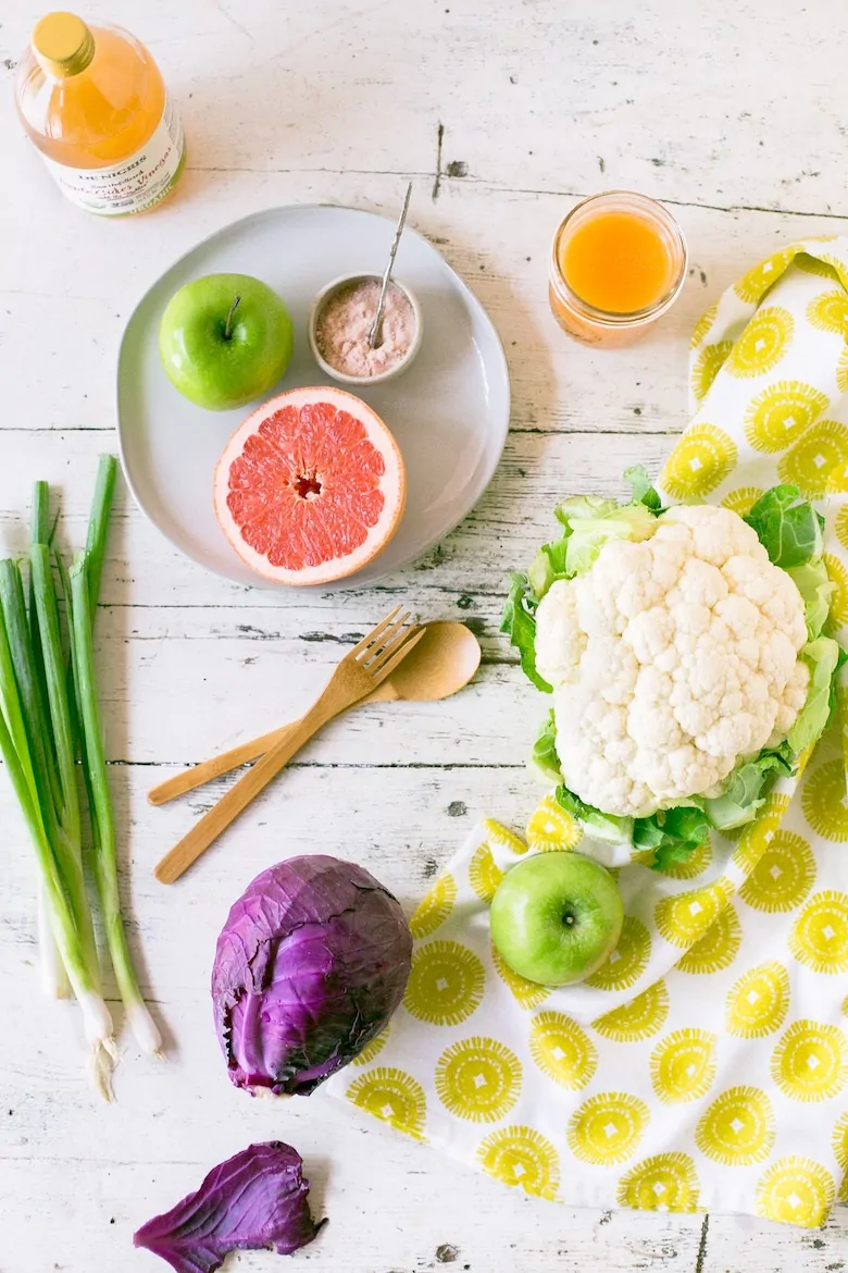 vegetables and fruits on a flat lay with a bottle and glass of orange juice