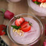 bowls of coconut strawberry mousse on a wooden round tray topped with fresh halved strawberries