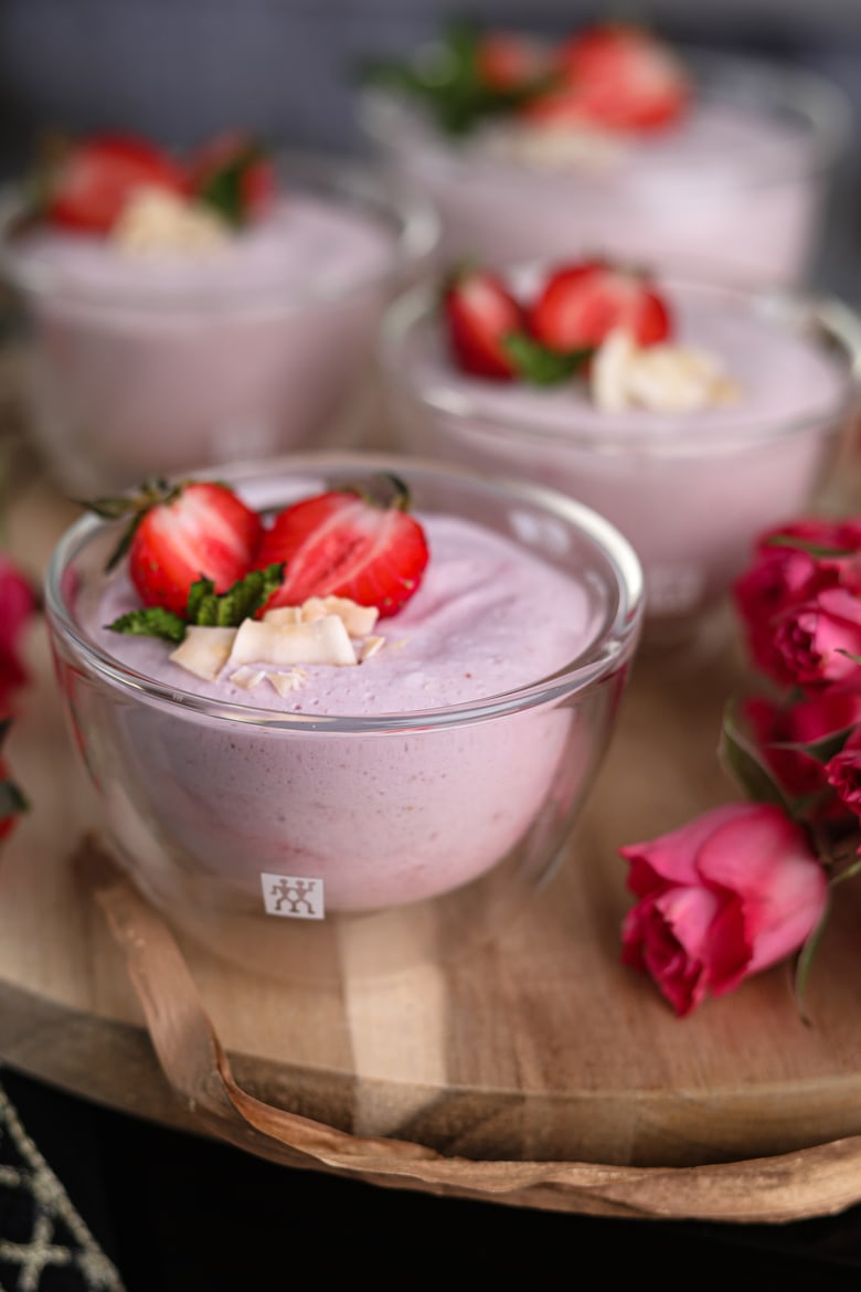 bowls of coconut strawberry mousse on a wooden round tray topped with fresh halved strawberries
