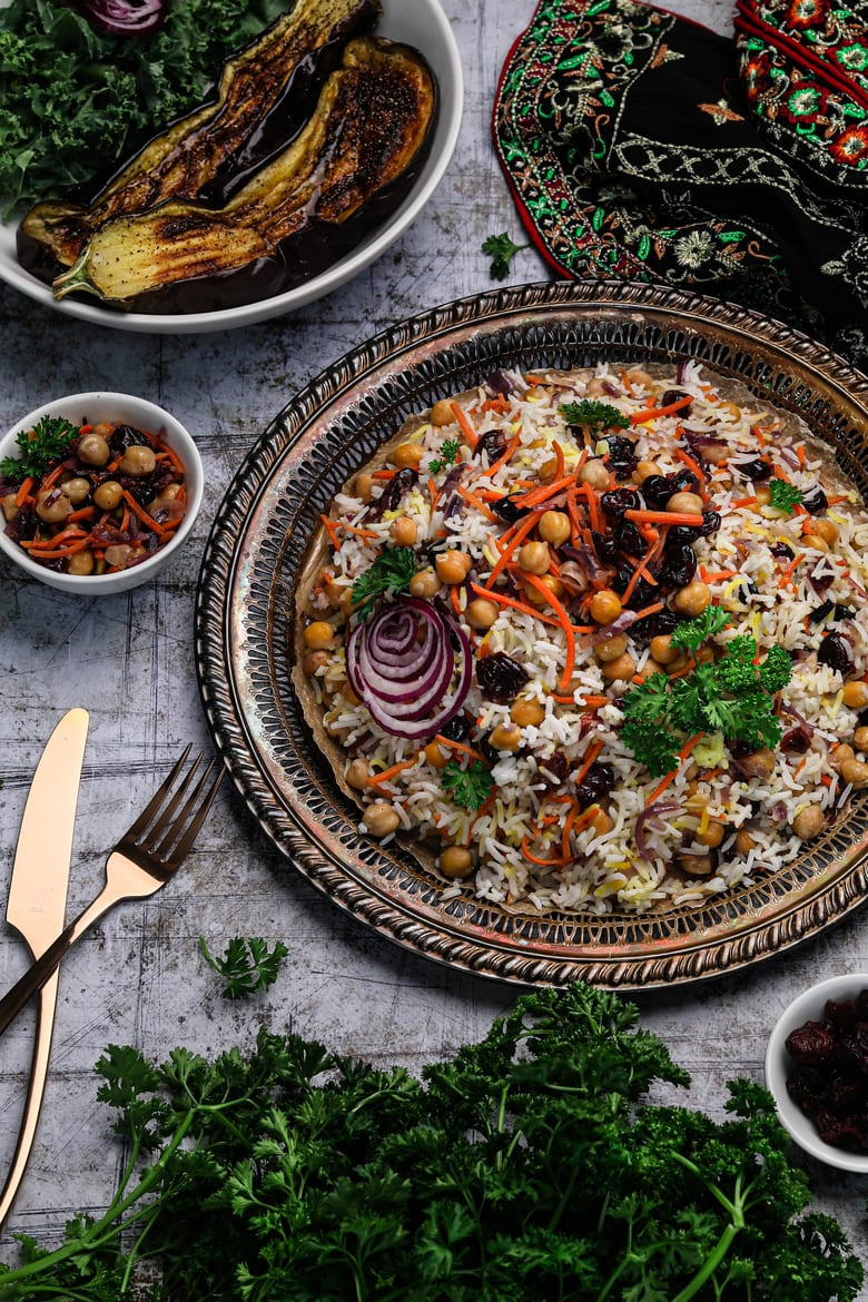 Persian rice in a round tray surrounded by fresh parsley, grilled eggplant and a traditional fabric