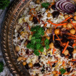 Persian rice in a round tray surrounded by fresh parsley, grilled eggplant and a traditional fabric
