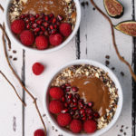 two bowls of chocolate and pumpkin smoothie breakfast topped with raspberries, pomegranate and nuts