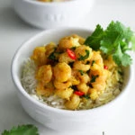 two bowls of coconut shrimp curry on a bed of basmati rice garnished with fresh cilantro leaves
