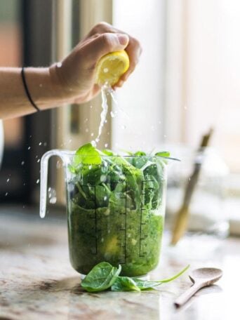 a person's hand squeezing a lemon into a jog of green spinach and juice