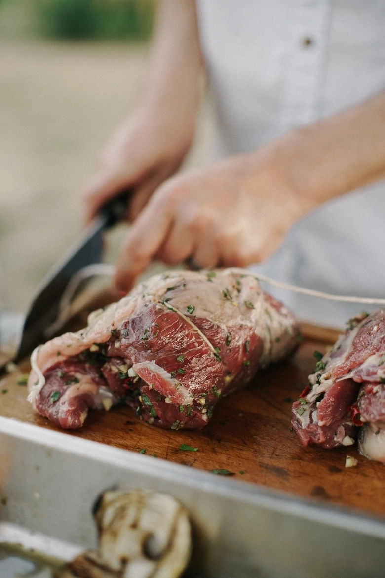 hands cutting red meat with a knife on a wooden board