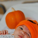 a baby lying on a blanet with an expression wearing a Halloween hat