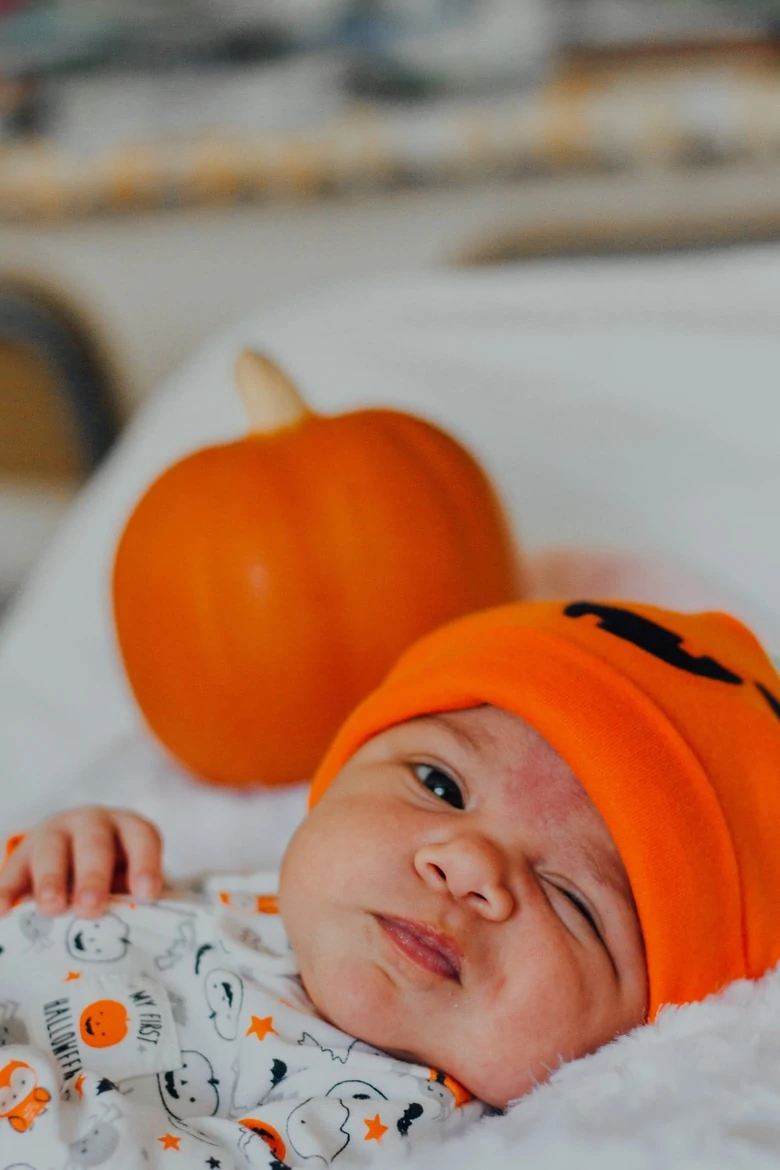 a baby lying on a blanet with an expression wearing a Halloween hat