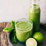 a bottle and glass of green juice in a tray with a couple of limes and spinach leaves