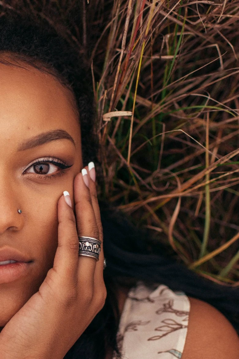 a woman of colour lying on a stack of hay touching her face looking serious about body shaming