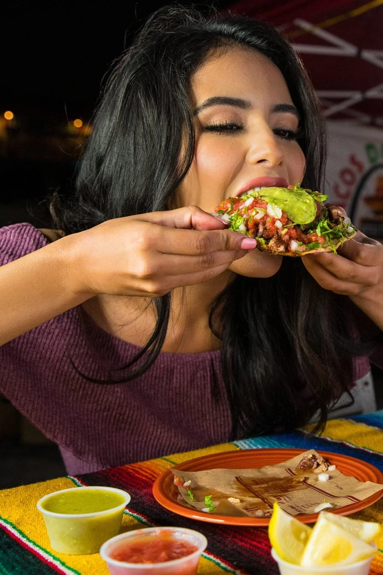 a woman of colour biting into a taco filling with vegetables, overeating due to stress of body shaming