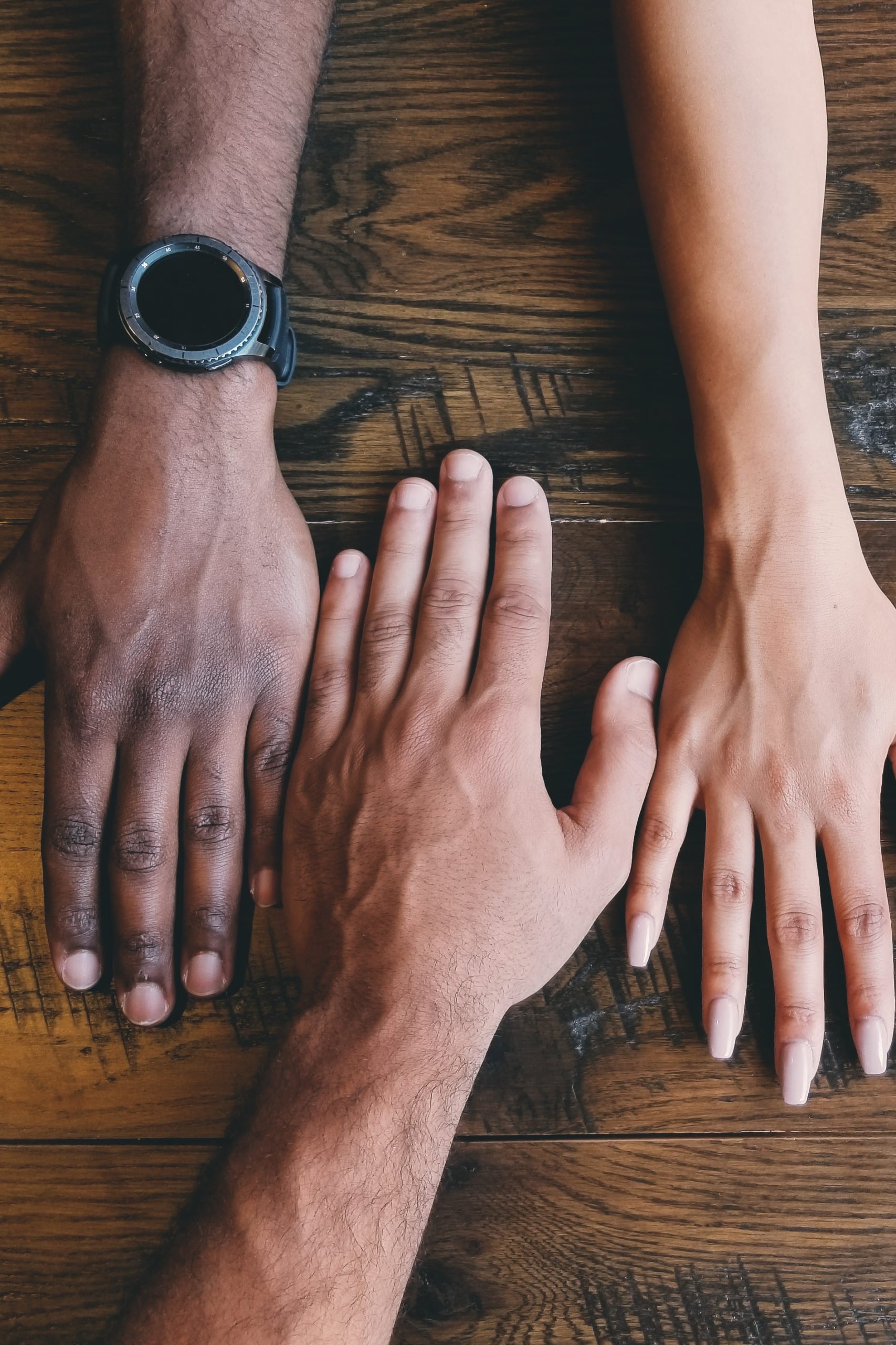 three hands of different people faced down on a wooden table