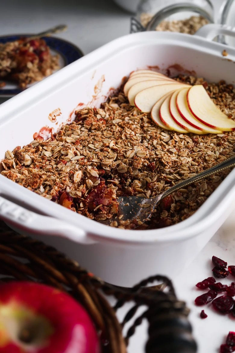 dish with cranberry apple crumble topped with sliced apples with dried cranberries and apple in the foreground